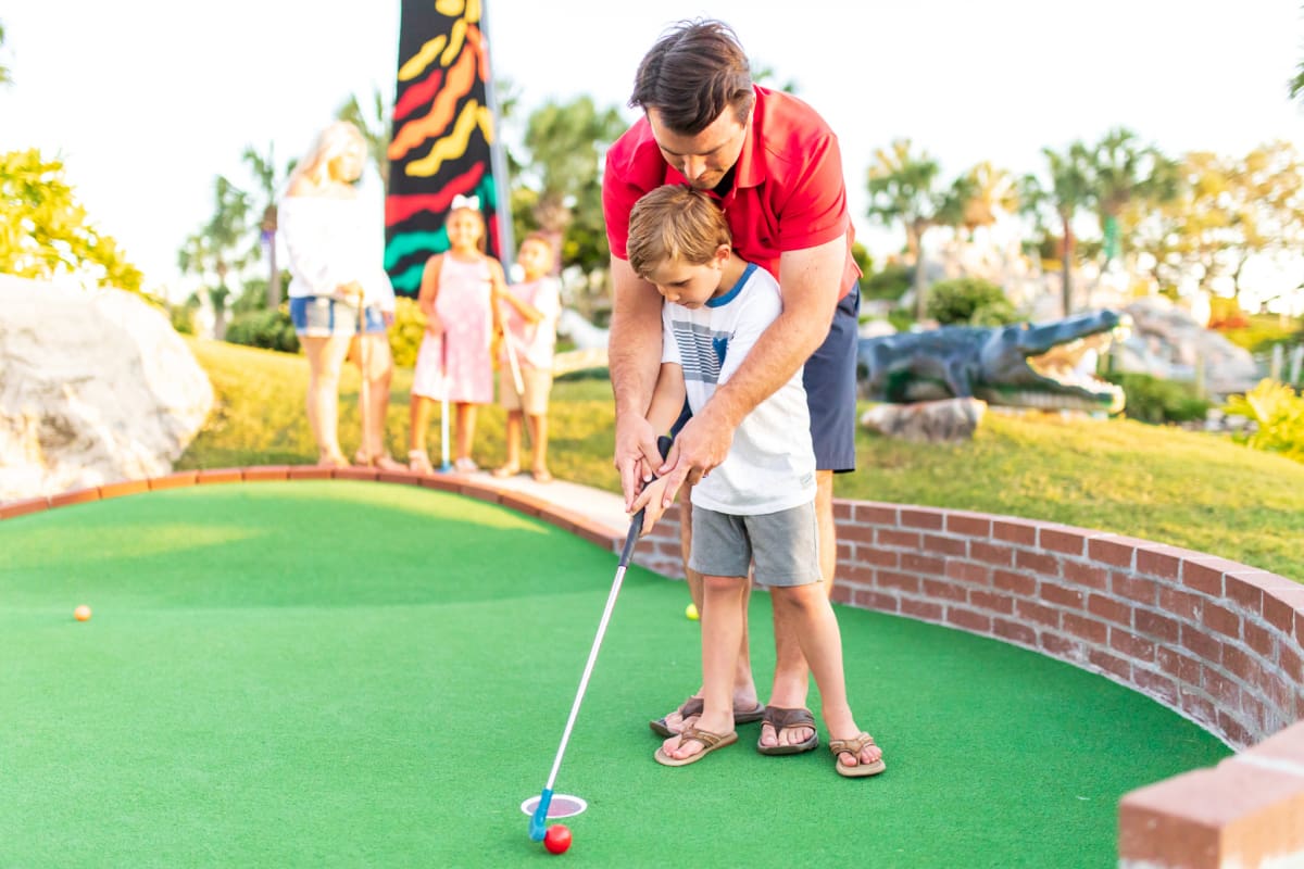 Image of a man helping a child make a putt.